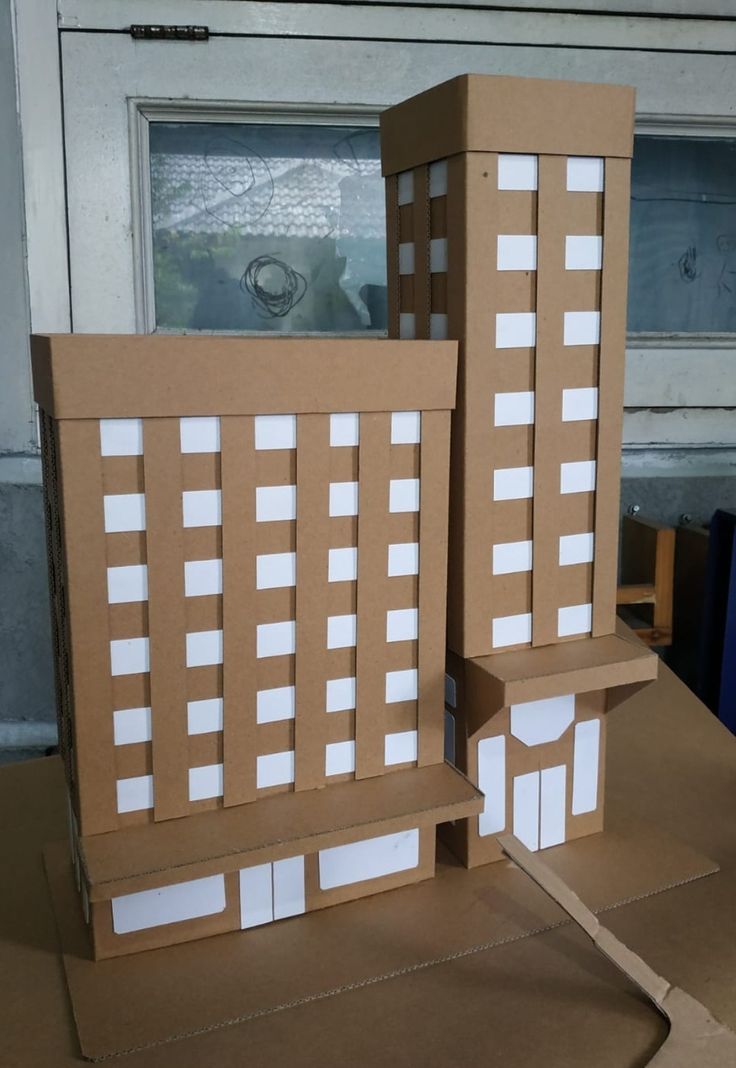 two cardboard buildings made to look like they are sitting on top of each other in front of a window