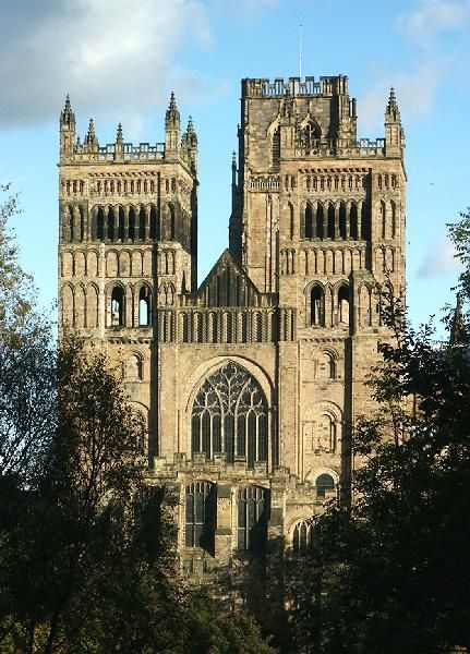 an old building with two towers and trees in the foreground on a sunny day