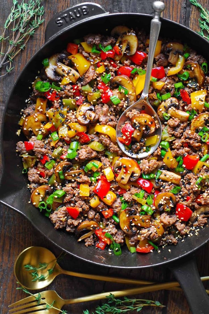 a skillet filled with meat and vegetables on top of a wooden table next to utensils