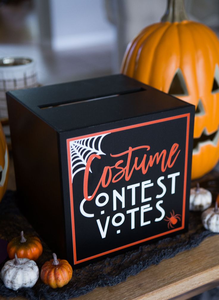 a costume contest box sitting on top of a table with pumpkins and other decorations