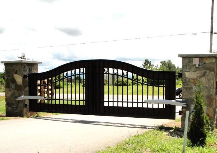 an iron gate and stone pillars are in front of a driveway with a bench on the other side