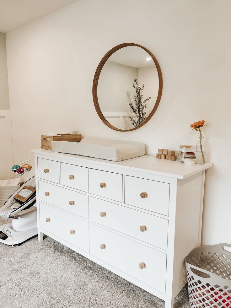 a white dresser with drawers and a mirror on the wall in a room that has carpeted flooring