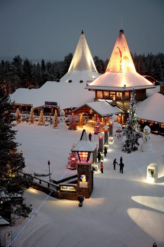 people are walking through the snow in front of a lit up christmas tree and building