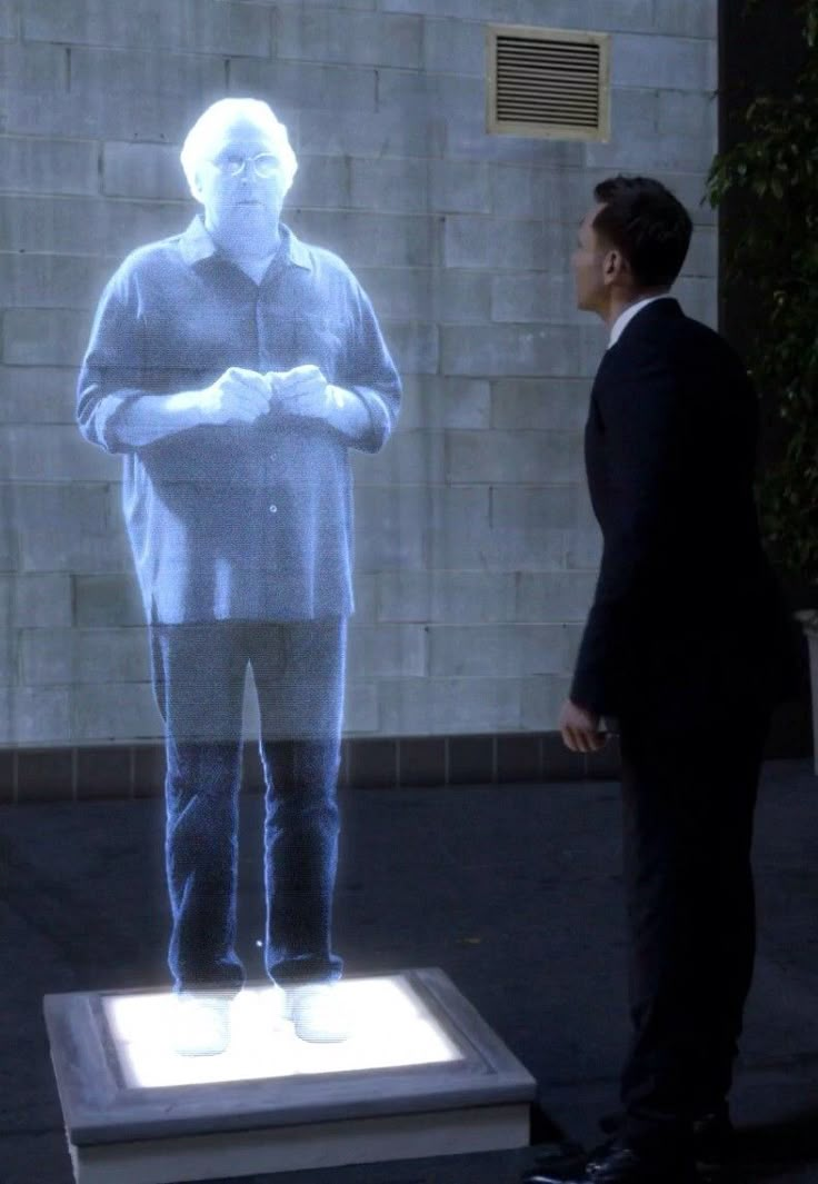 a man standing in front of a projected image of a man with his hands folded