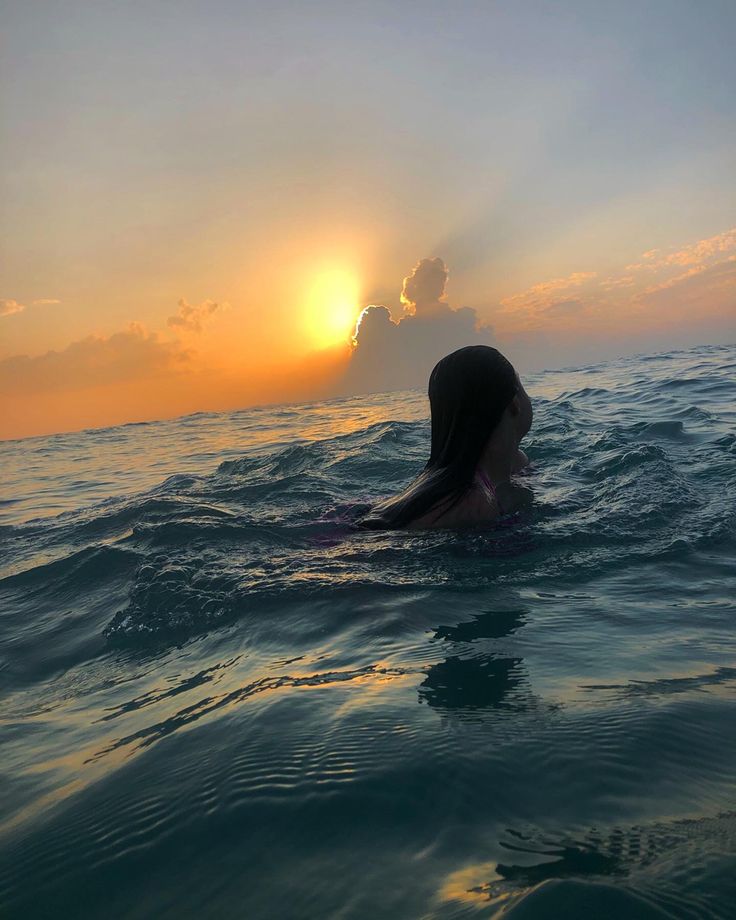 a woman swimming in the ocean at sunset with her head above water's surface