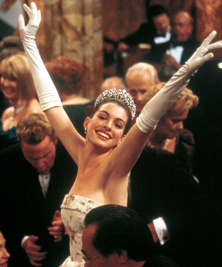 a woman wearing a tiara and holding her arms up in the air at an event