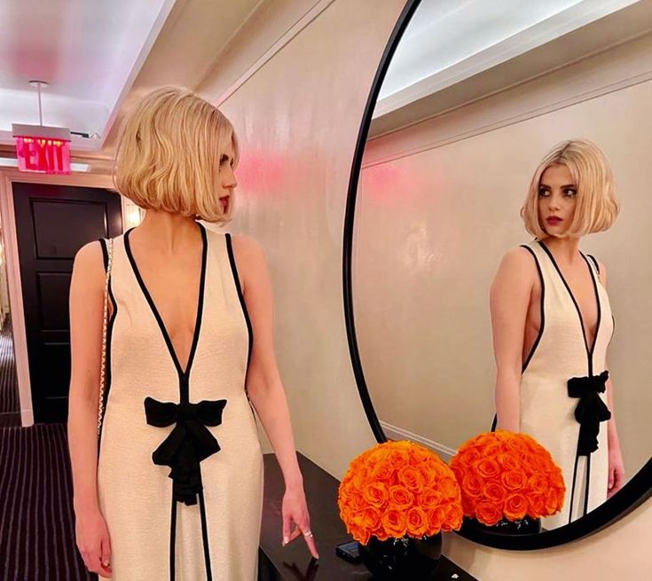 a woman standing in front of a mirror holding an orange flower bouquet and looking at herself in the mirror