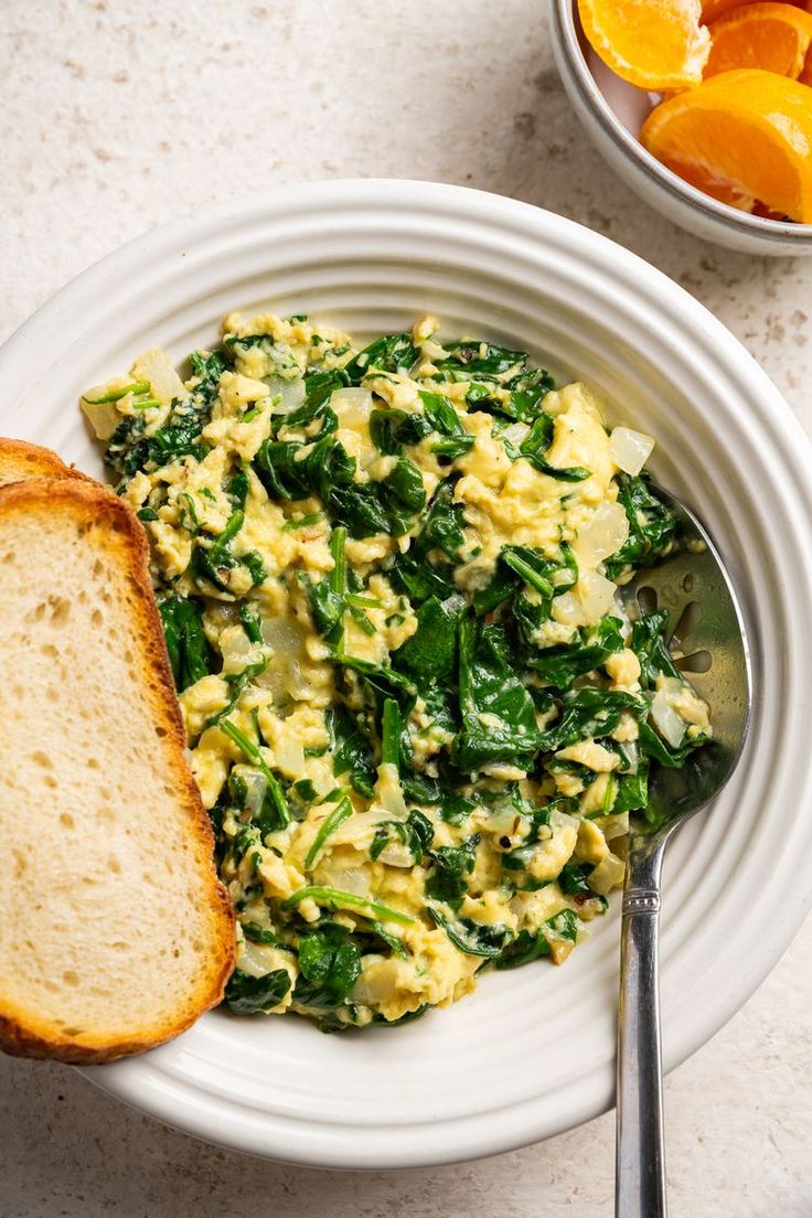 an egg salad with spinach and bread on a white plate next to orange slices