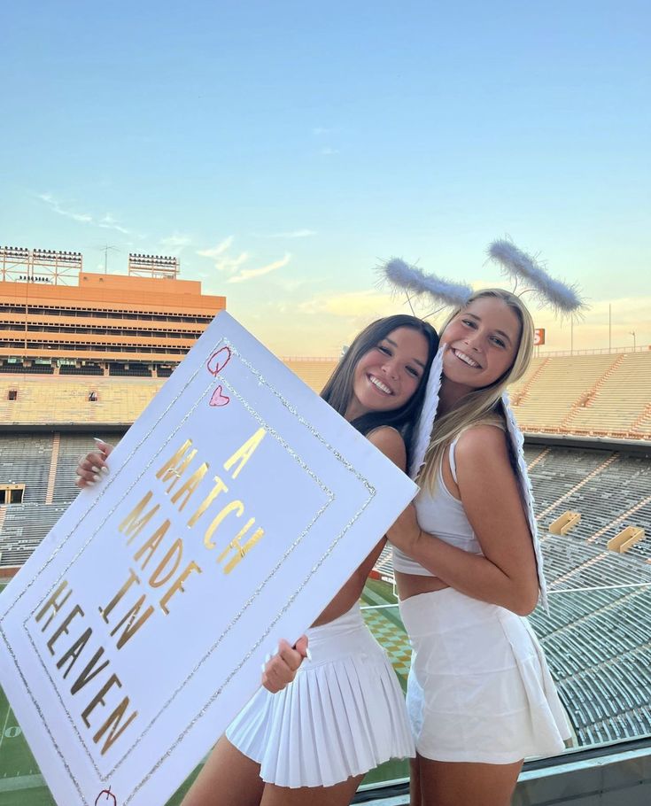 two girls are holding up a sign in front of an empty stadium bleachers