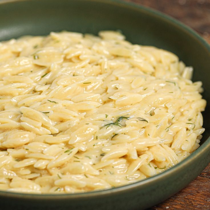 a green bowl filled with macaroni and cheese on top of a wooden table