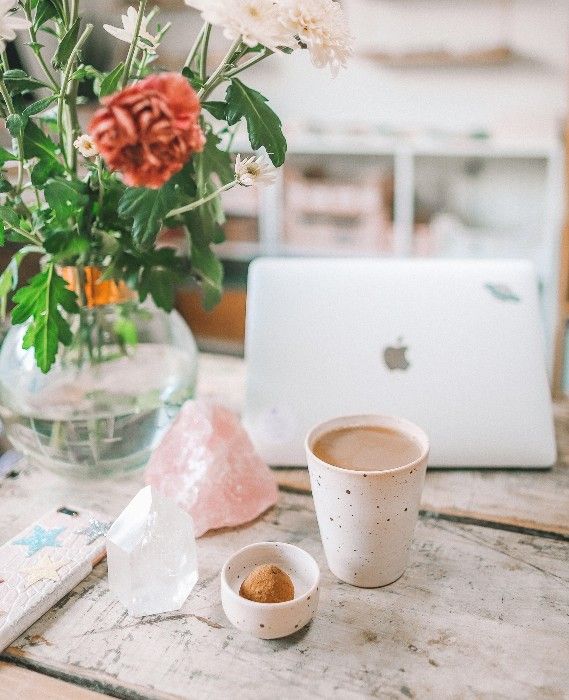 there is a vase with flowers on the table next to two cups and a laptop