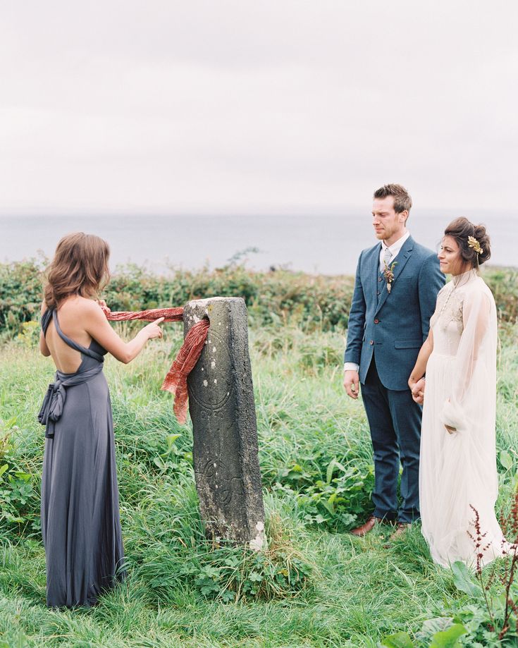 a man and woman standing next to each other in the grass near a stone pillar