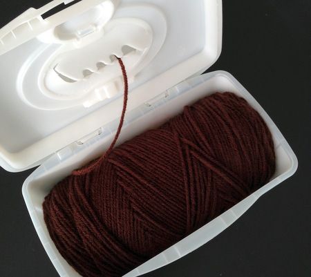 a spool of red yarn in a white container on a black surface next to a pair of scissors