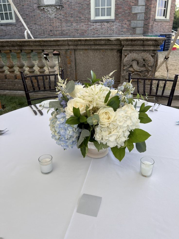 a vase with white flowers and greenery on a table in front of a building