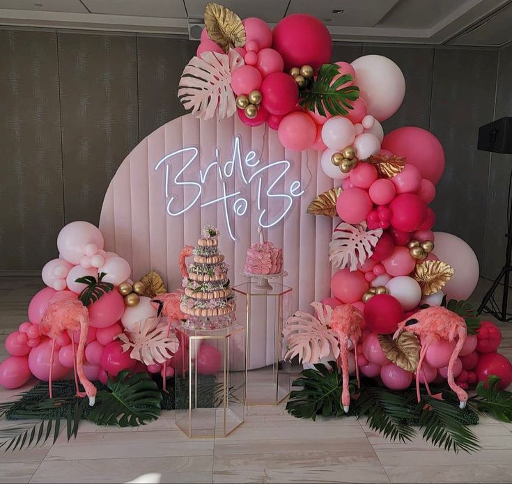 a pink and gold wedding cake surrounded by flamingos, palm leaves, and balloons