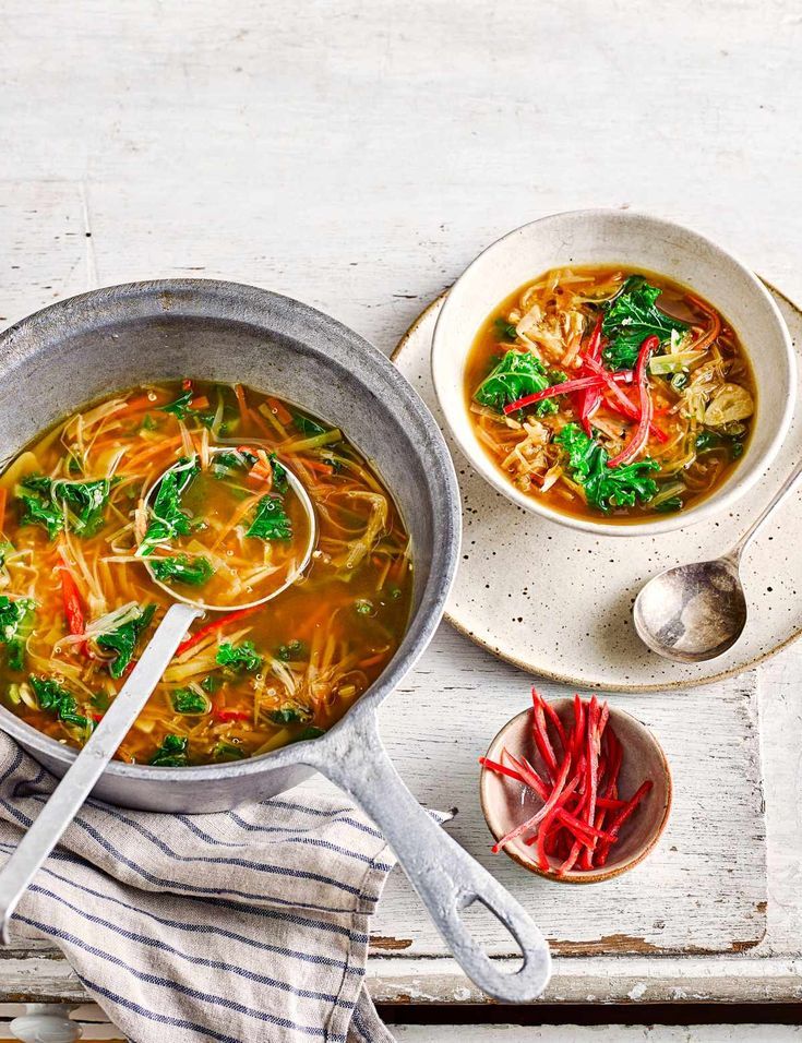 a bowl of soup with broccoli, noodles and red peppers on a white table