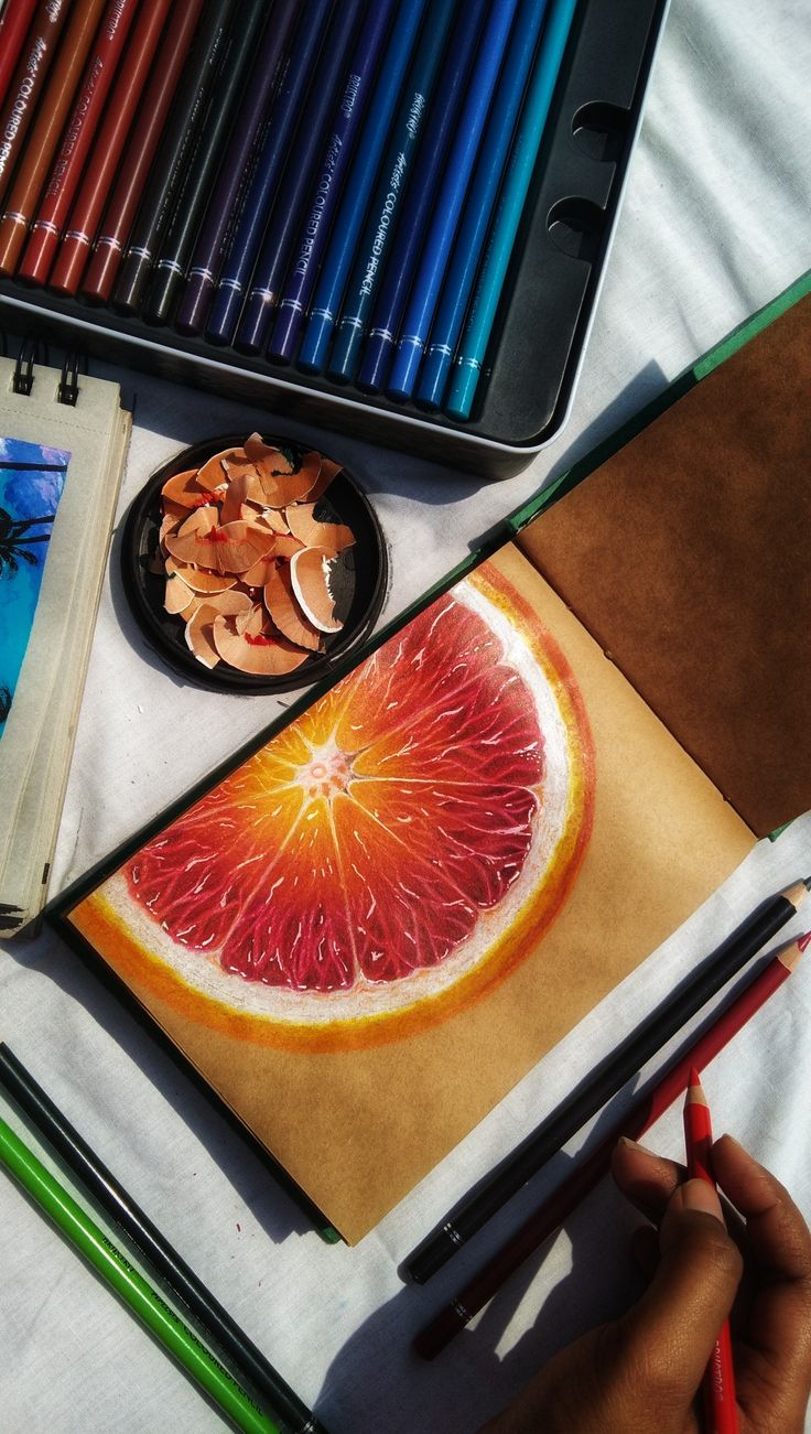 a grapefruit cut in half next to colored pencils and other art supplies