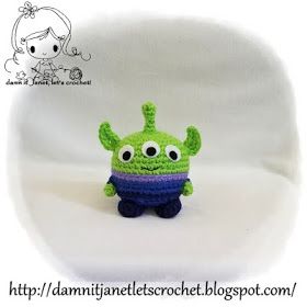 a small crocheted green alien with big eyes sitting on a white surface and looking at the camera