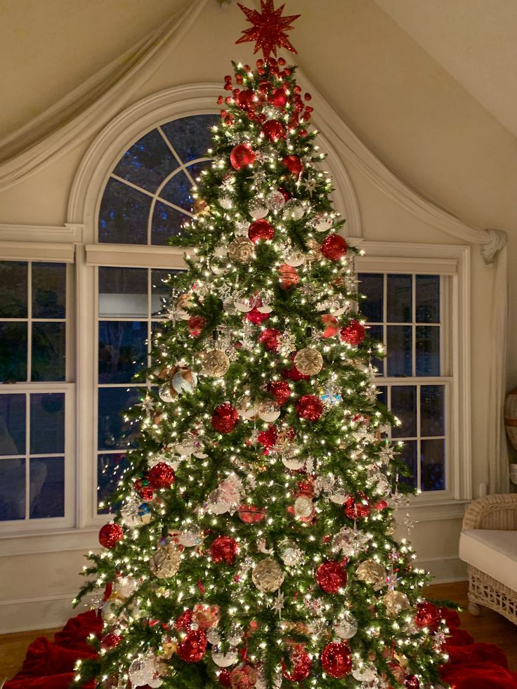 a decorated christmas tree in front of a window with red and white ornaments on it