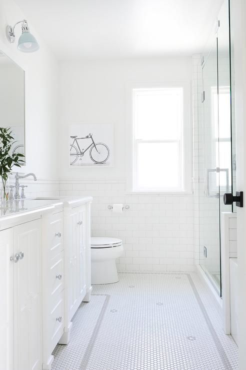 a bathroom with white tile floors and walls, along with a large mirror on the wall