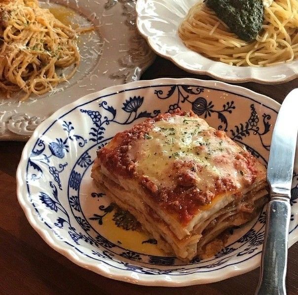 a plate with lasagna on it next to some pasta and broccoli