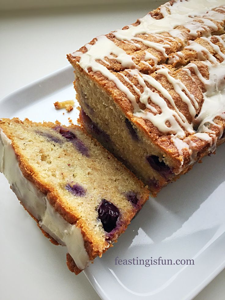 a loaf of blueberry bread on a white plate with icing and drizzled