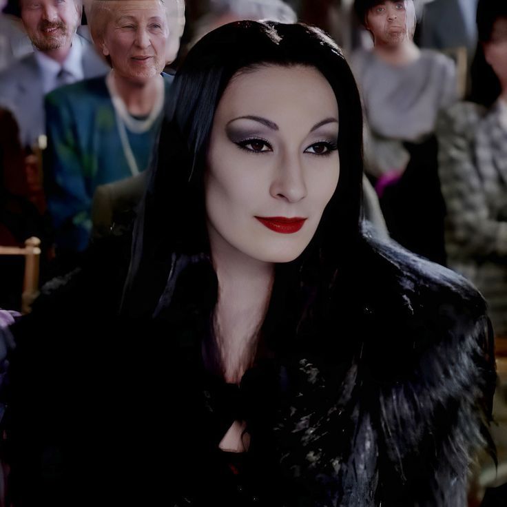 a woman with long black hair and red lipstick sitting in front of an older man