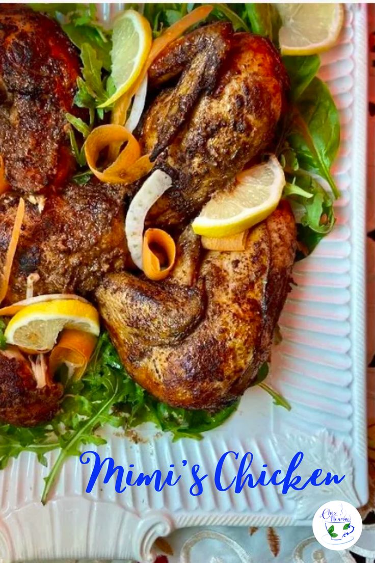 a white plate topped with meat covered in lettuce and lemon wedges on top of a table