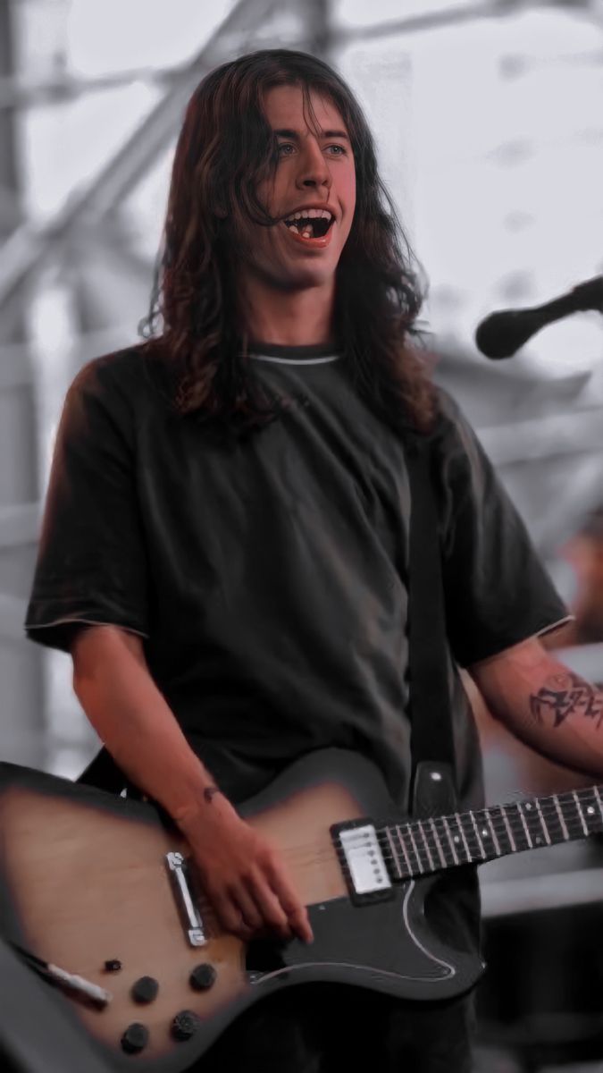 a man with long hair holding a guitar and singing into a microphone at an outdoor concert