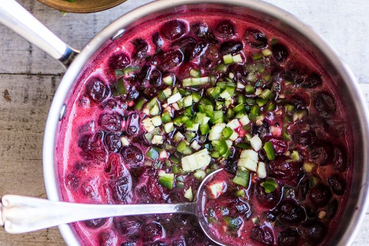 a pot filled with blueberries and celery next to two spoons on a table