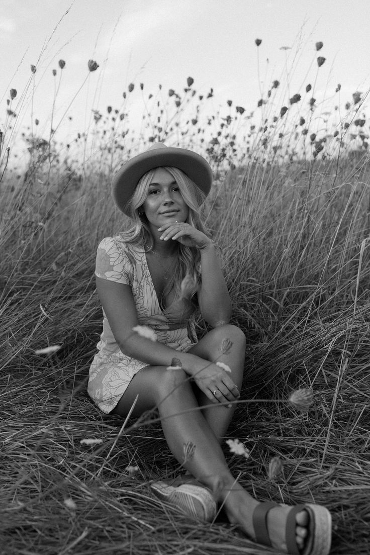 a woman sitting in the middle of a field wearing a hat