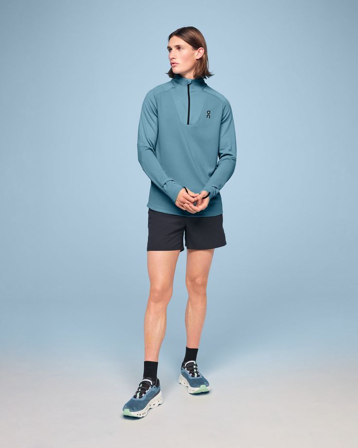 a woman standing in front of a blue background wearing black shorts and a green hoodie