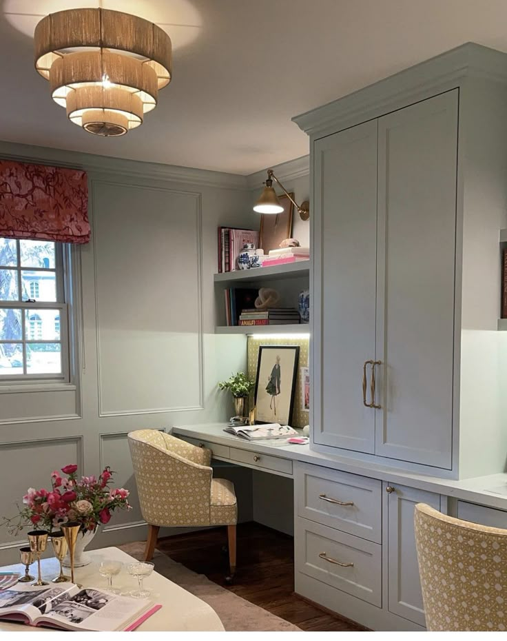 a desk with two chairs and a book shelf in front of it, next to a window