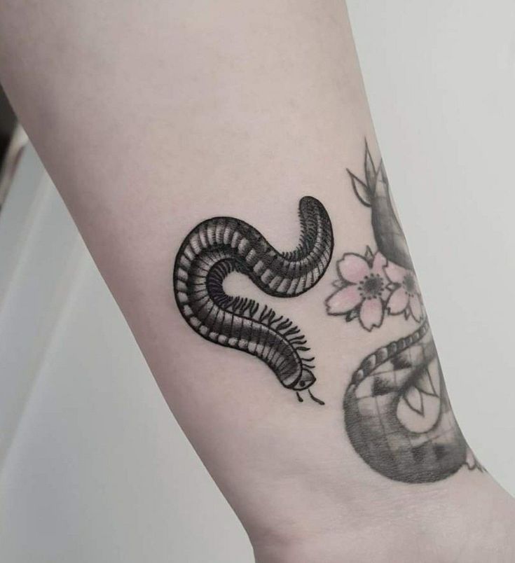 a black and white snake tattoo on the left side of the arm, with flowers in the background