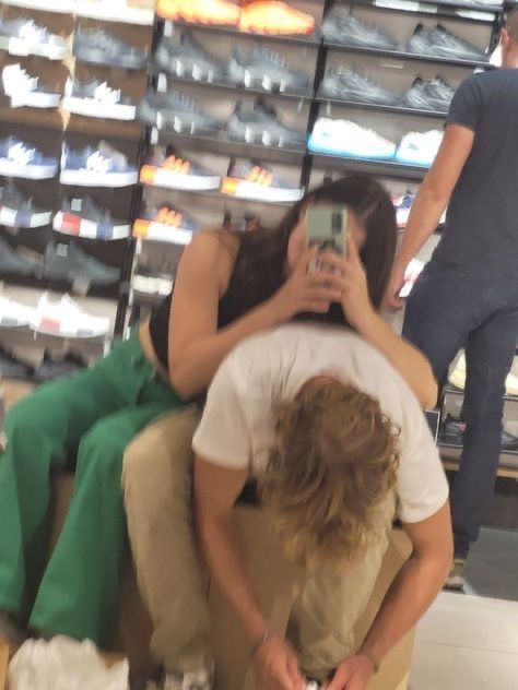 two people sitting on a chair in a shoe store taking pictures with their cell phones