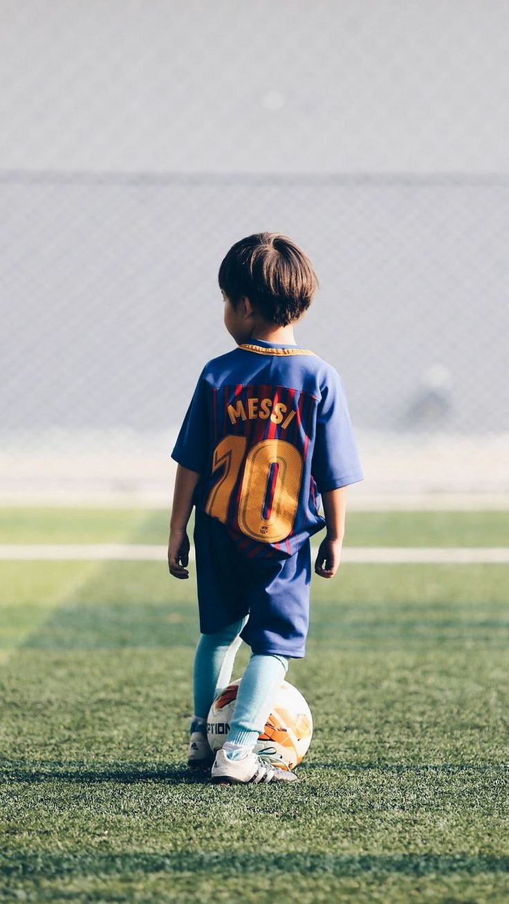 a little boy that is standing in the grass with a soccer ball on his feet