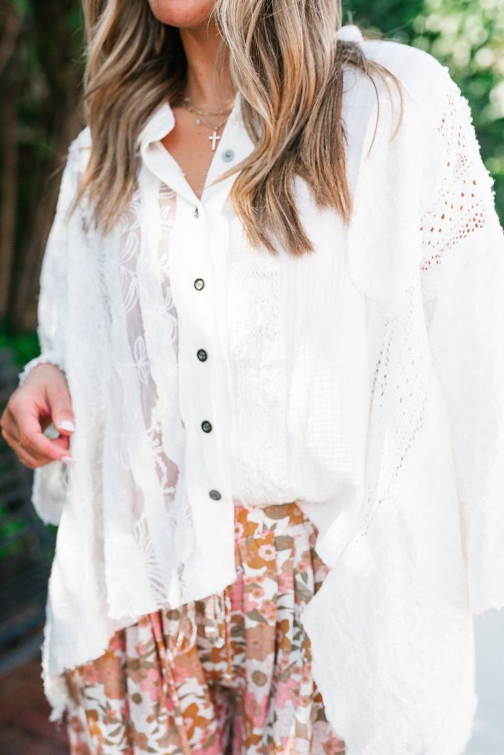 The Lakelyn Lace Ivory Button Up Top is a beautifully crafted, off-white lace and gauze blouse that exudes a romantic, bohemian vibe. The top features a delicate mix of lace and textured fabric, creating a soft and airy look perfect for layering. It has a button-down front with small, dark buttons that add a subtle contrast to the light fabric. The collar is slightly frayed, contributing to its relaxed and effortless style. The sleeves are voluminous and made entirely of intricate lace, adding a Day Out Lace Blouse With Lace Trim, Bohemian Blouse With Lace Sleeves, White Bohemian Crochet Top For Day Out, White Lace Patchwork Top For Brunch, Feminine Summer Lace Top With Lace Cuffs, White Lace Top With Patchwork For Day Out, Flowy Lace Bohemian Blouse, Feminine White Blouse For Layering, Bohemian Lace Top With Lace Trim For Layering