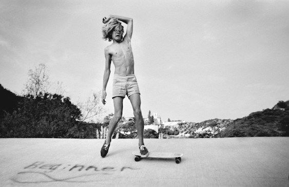 a shirtless man riding a skateboard on top of a cement ground next to trees