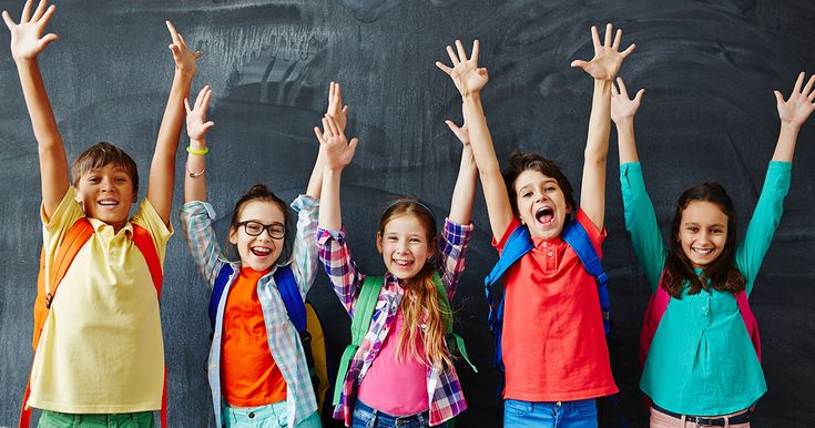 group of children standing in front of blackboard with their arms up and hands raised