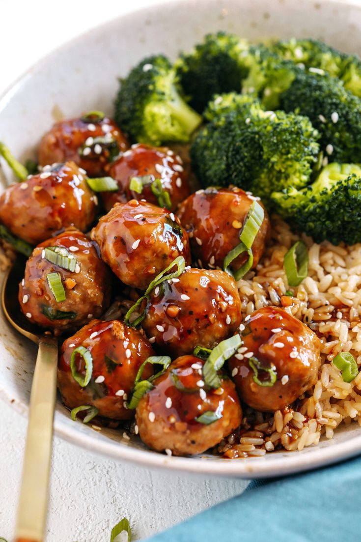 a white bowl filled with meatballs and broccoli on top of brown rice