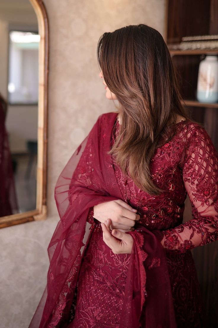 a woman in a red dress looking at herself in the mirror and holding her hand on her hip