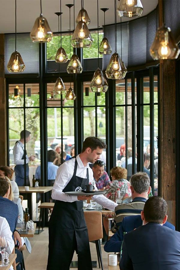 a waiter is standing in front of a group of diners at a restaurant with lights hanging from the ceiling