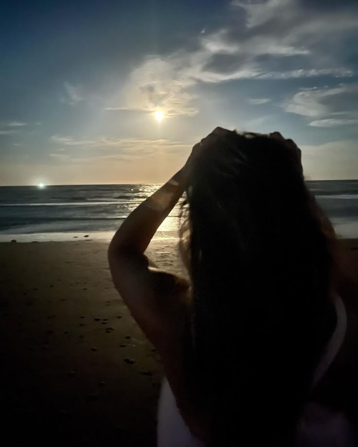 a woman standing on top of a beach next to the ocean under a cloudy sky