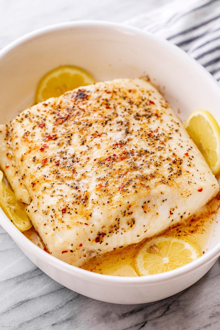 a close up of a fish in a bowl with lemons and seasoning on the side