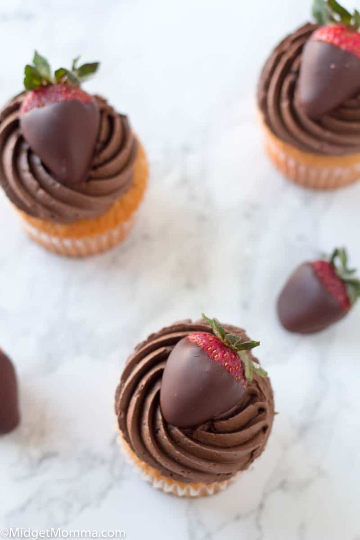 chocolate cupcakes topped with strawberries on a marble counter top, ready to be eaten