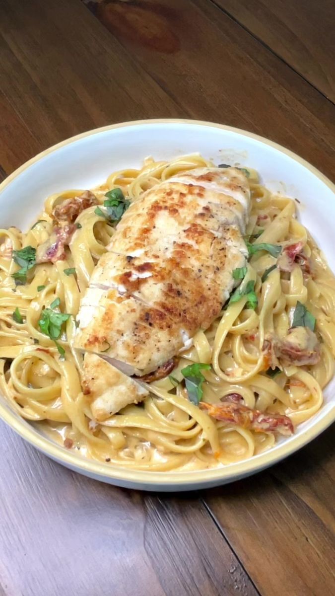 a white plate topped with chicken and pasta on top of a wooden table next to a fork