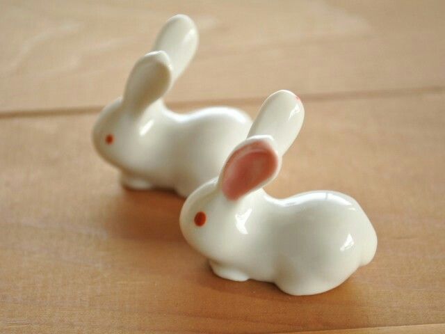 two white ceramic rabbits sitting on top of a wooden table