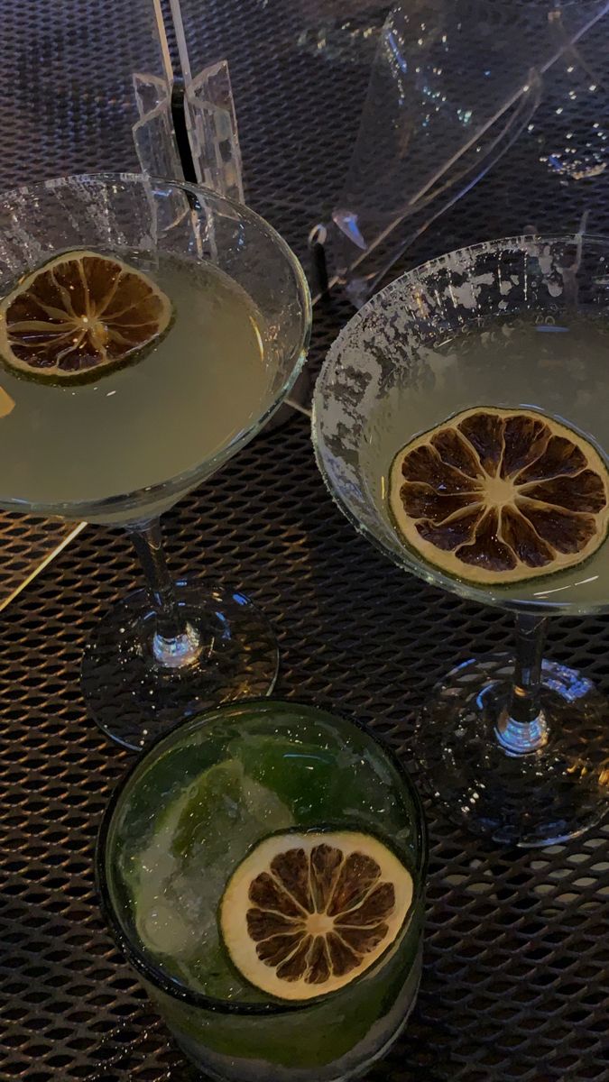 two glasses filled with liquid and some slices of lemon on the rims next to each other