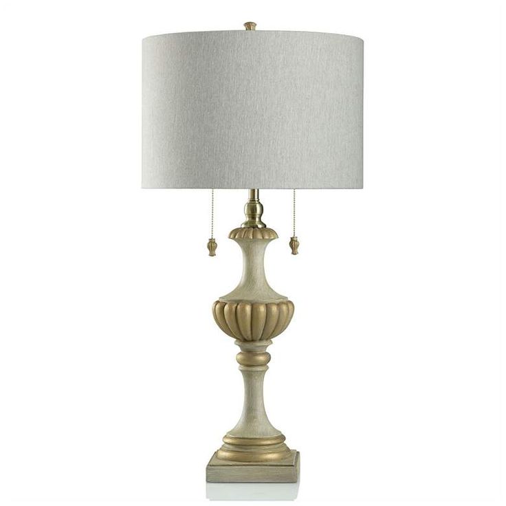 a lamp with a white shade on top of it and a gold finish around the base