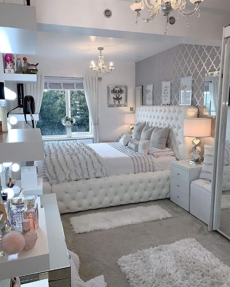 a bedroom with white furniture and chandelier hanging from the ceiling in front of a large mirror